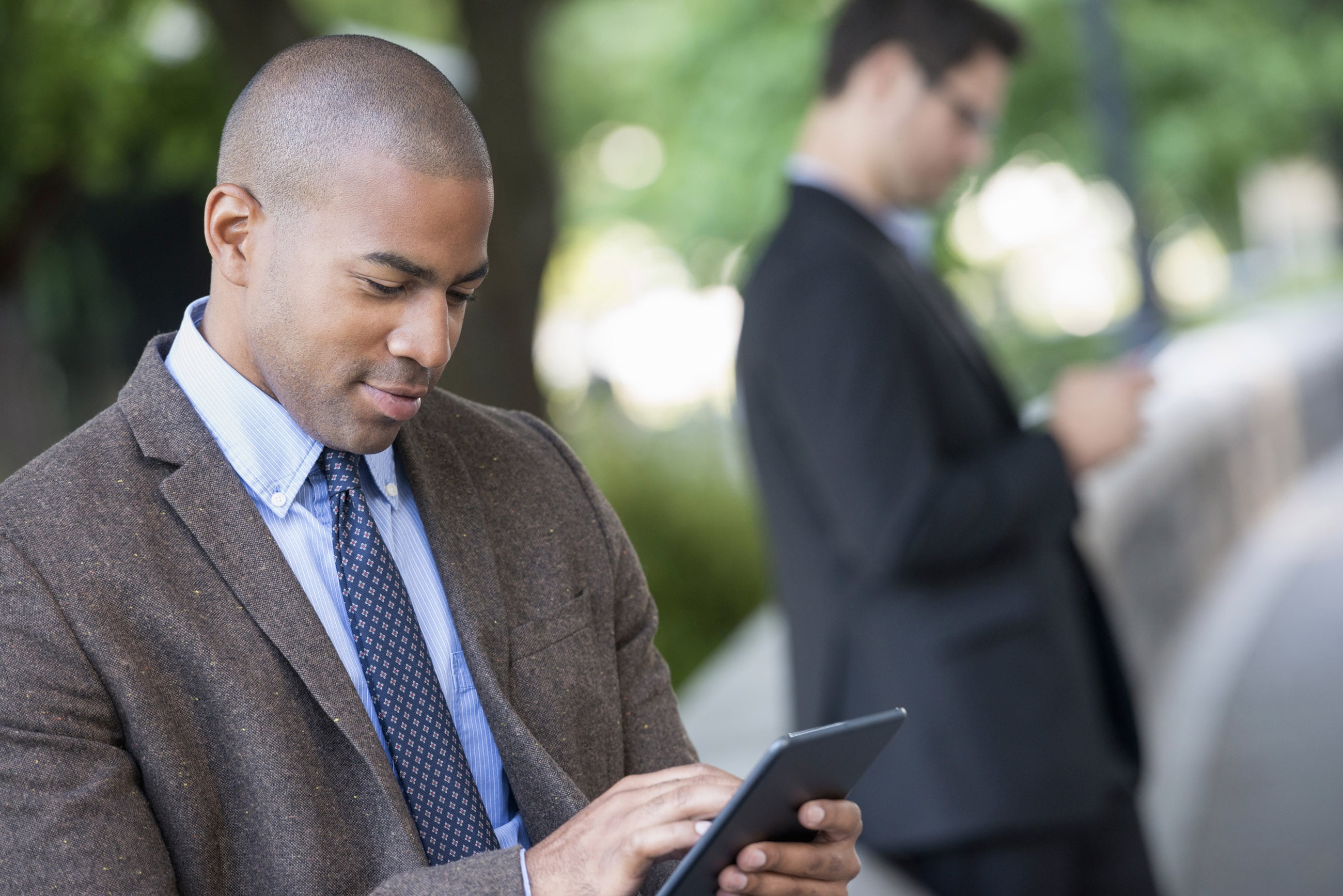 Two men in suits standing outside looking at their phones