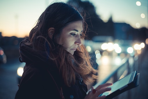 Lady standing outside at night looking at tablet