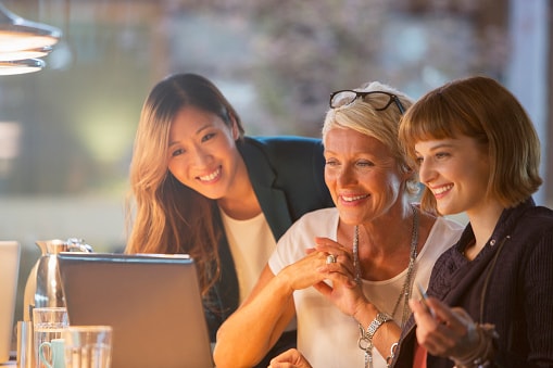 Three ladies looking at laptop sitting around a table 