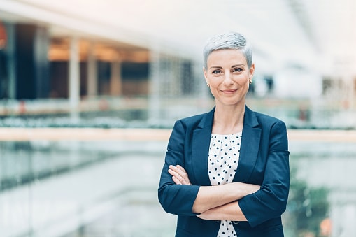 Lady with short grey hair in blue suit standing in glass office