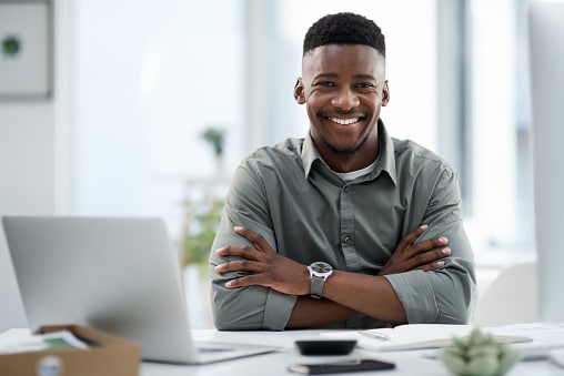 Man sitting a desk next to laptop with arms folded and watch on show