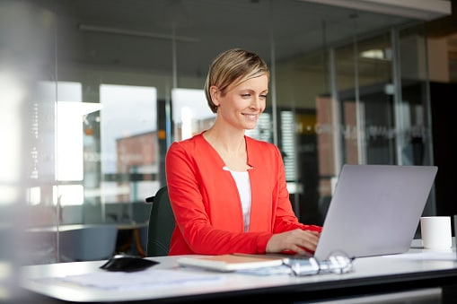 Lady in red shirt, sitting in front of laptop in office 