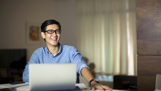 Man in blue shirt sitting behind a laptop in his home office