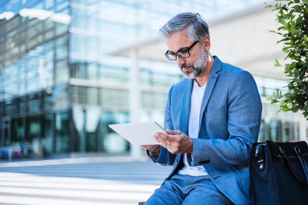 Man in blue blazer with grey hair and glasses looking at tablet