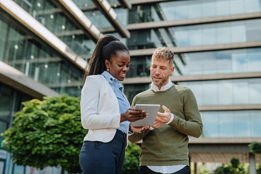 Man and lady standing outside a glass office looking at tablet