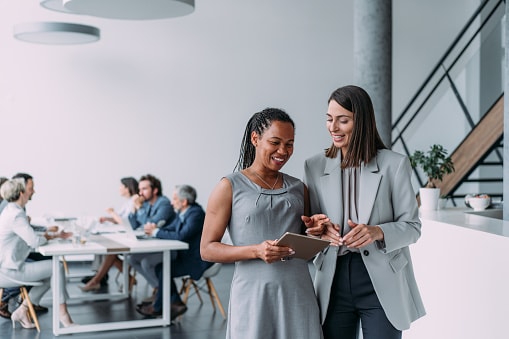 Two ladies wearing grey in office, looking at tablet