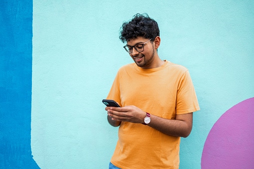 Man in orange Tshirt standing looking at his phone 