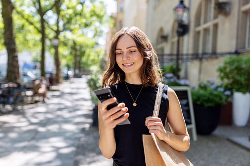 Lady walking down street, in black dress looking at her phone 