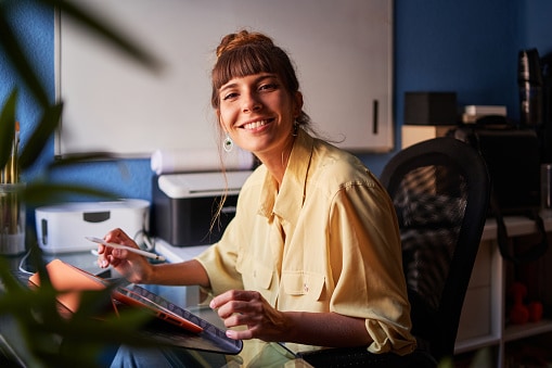 Lady sitting at desk in blue office, looking up and smiling 